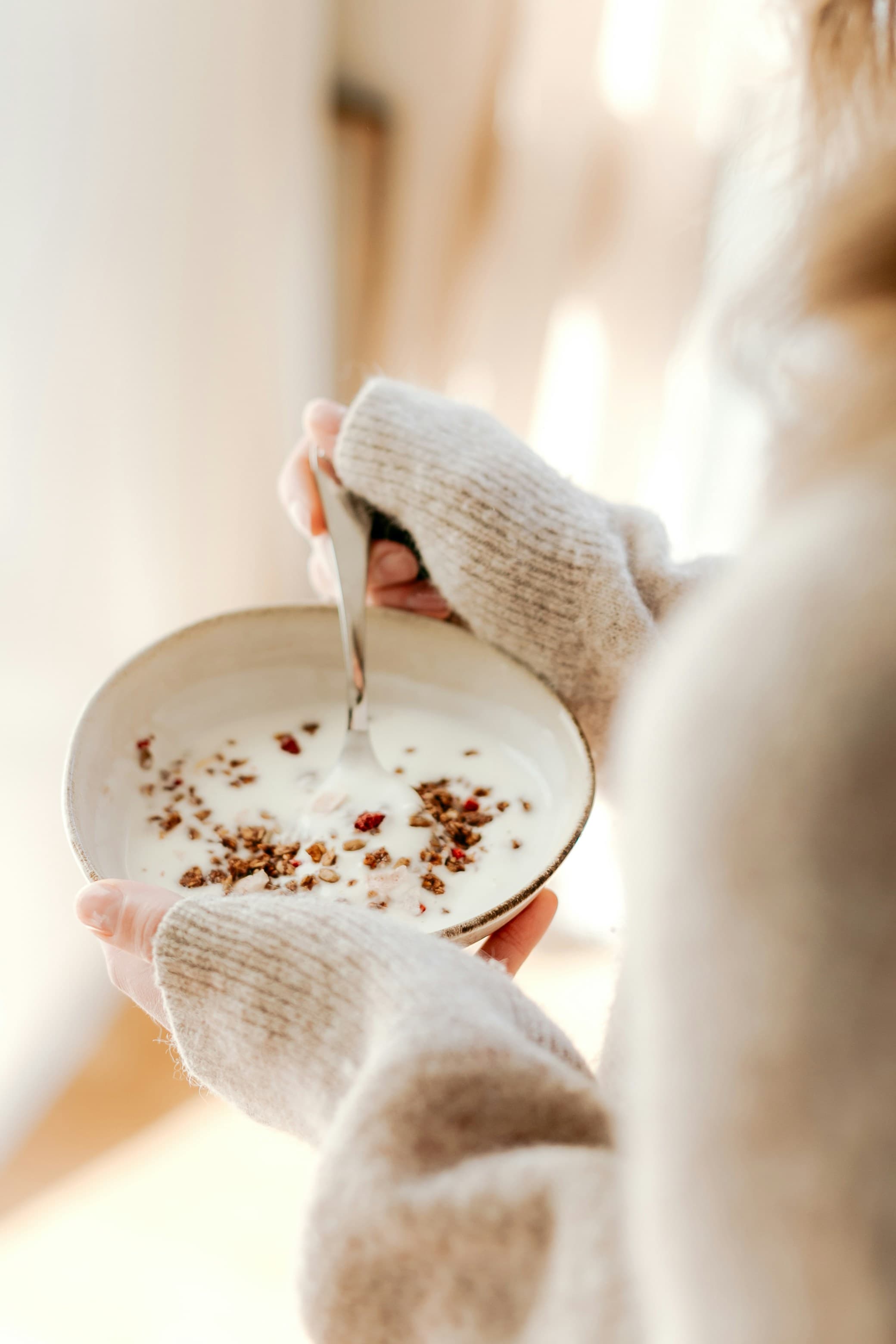 A woman holding a bowl of yogurt and granola in soft morning light