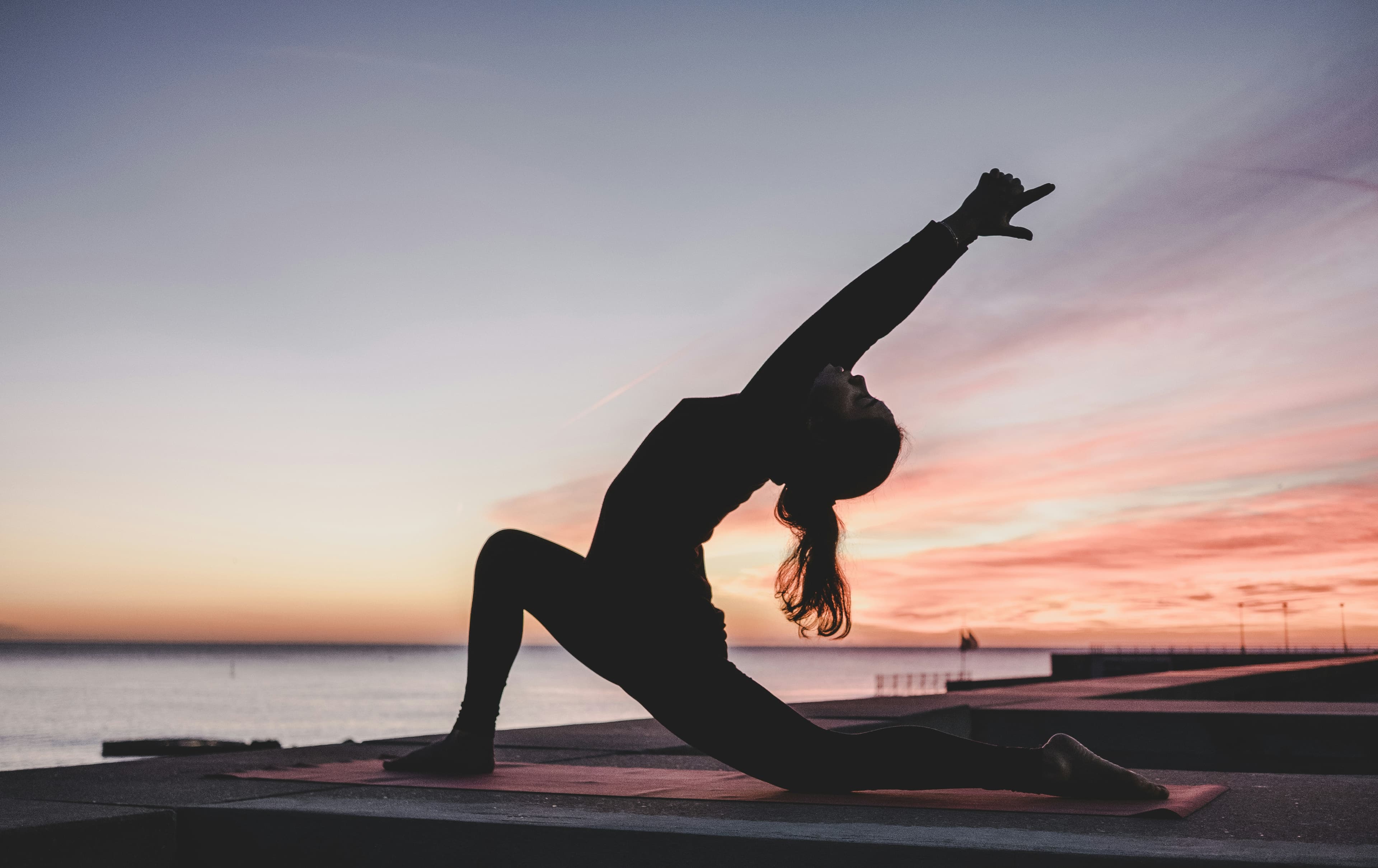 A woman stretching on a yoga mat at sunset — restored mobility beyond chronic pain