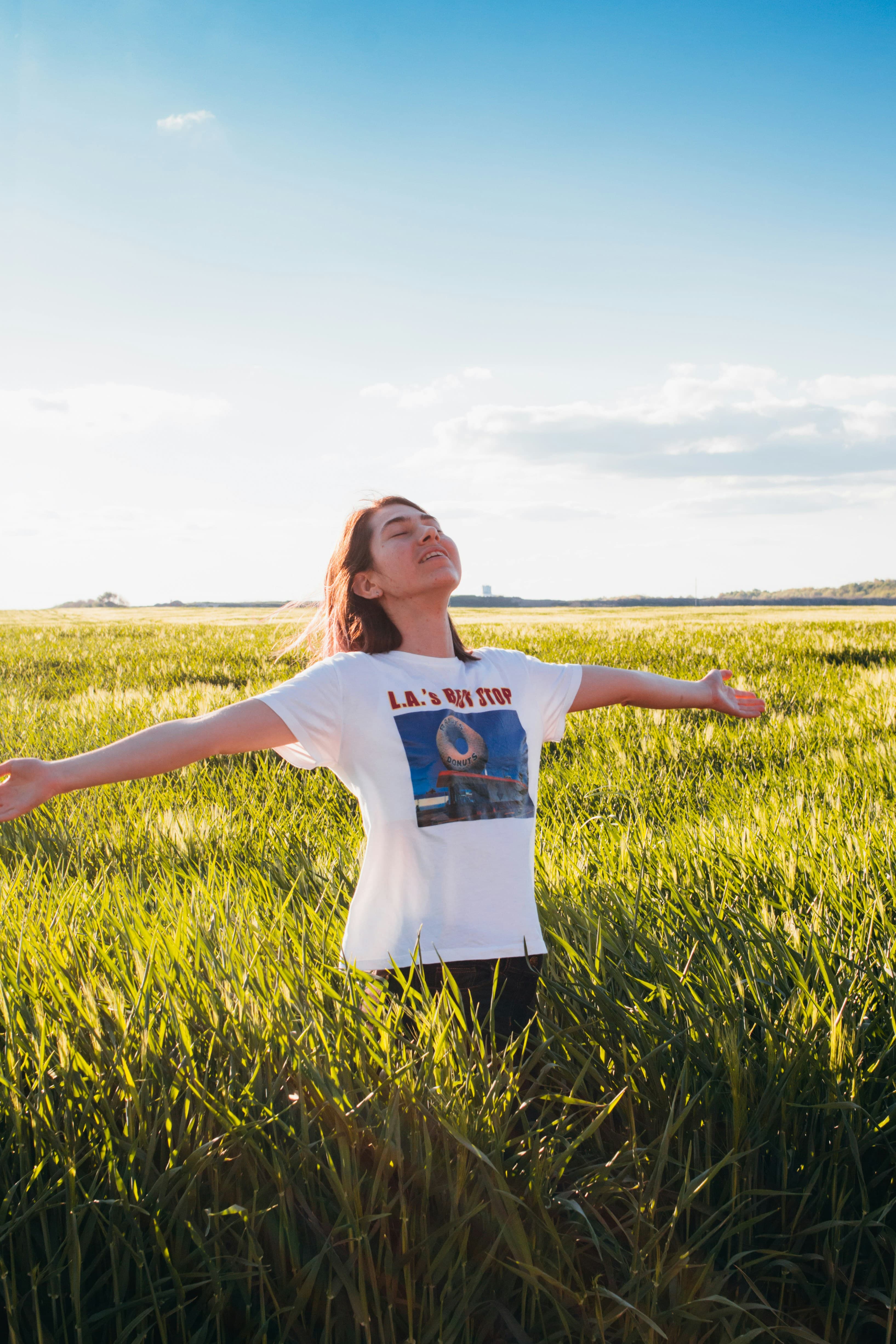 A woman standing arms-open in a sunlit field — relief and renewed quality of life